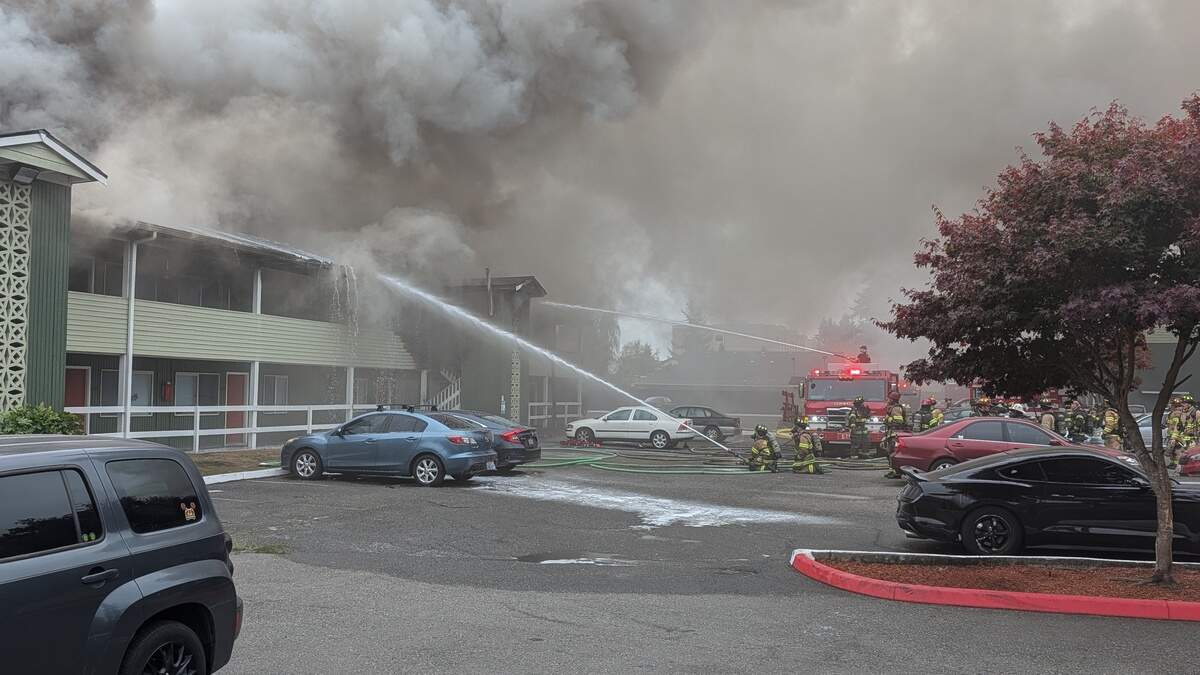 Firefighters spray water onto the smoke-filled second story of a two-story apartment building on Israel Road Southwest in Tumwater as fire engines and crews fill the parking lot
